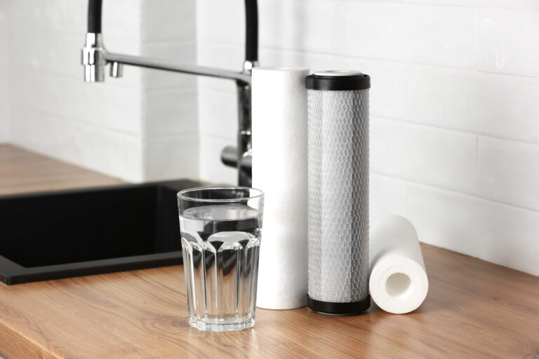 Glass of filtered water beside water filter cartridges on a kitchen counter, highlighting home water filtration.