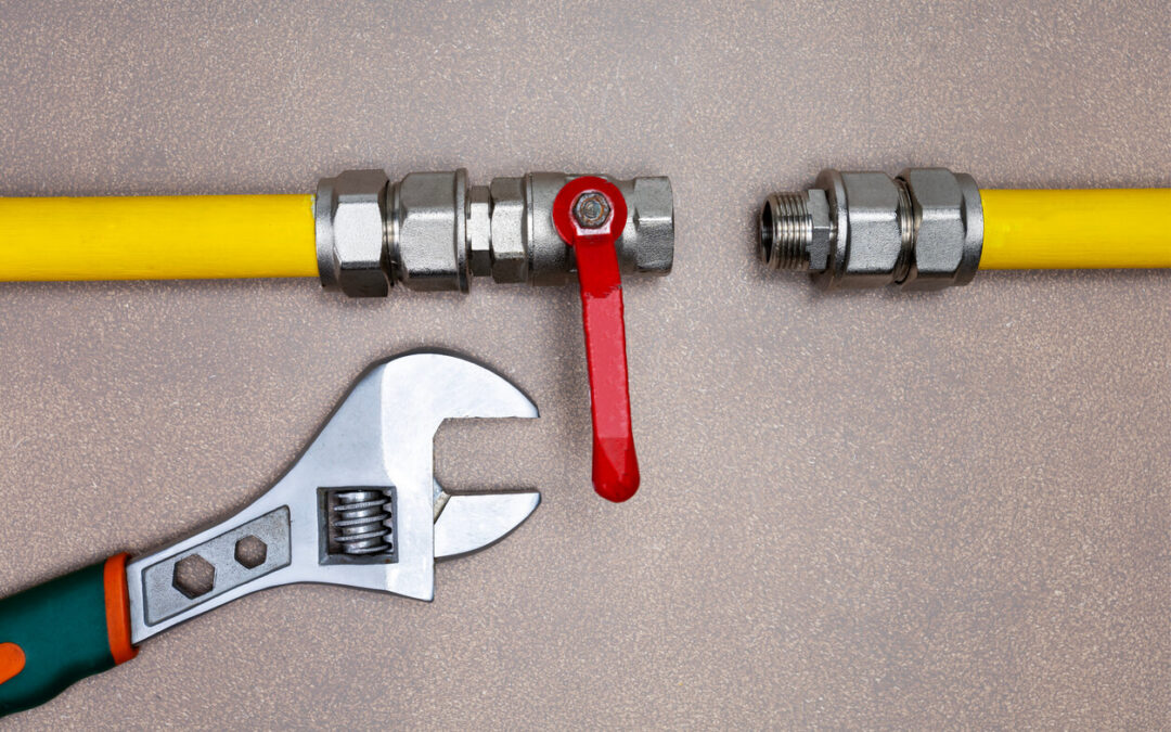 Gas pipeline with a disconnected metal valve and yellow pipe, accompanied by an adjustable wrench on a textured surface.