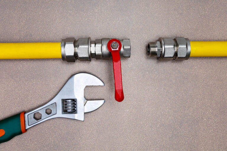 Gas pipeline with a disconnected metal valve and yellow pipe, accompanied by an adjustable wrench on a textured surface.