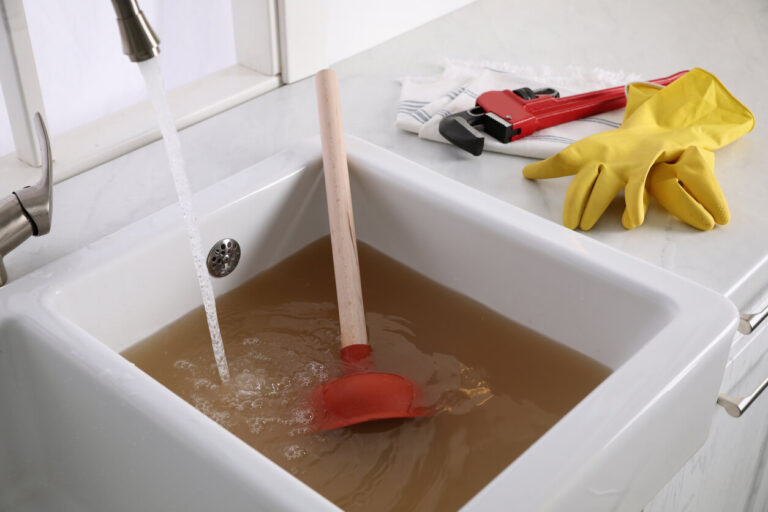 Standing dirty water in a clogged kitchen sink with plunger and gloves, highlighting DIY vs professional drain cleaning in Greater Houston.