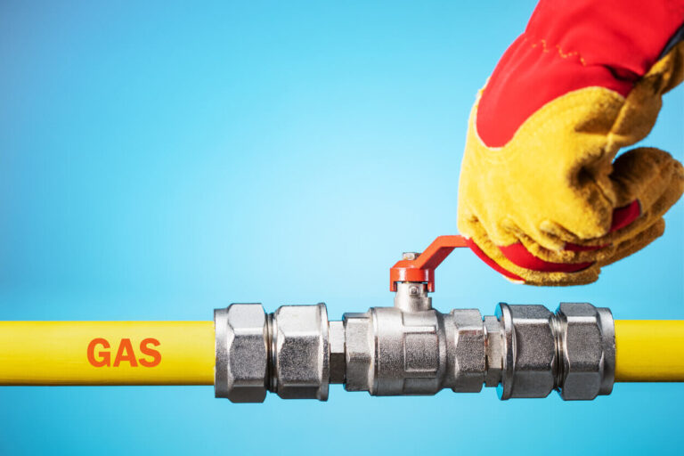 Technician turning valve on yellow gas pipe with protective gloves, safety check for gas line repair in Houston, Texas