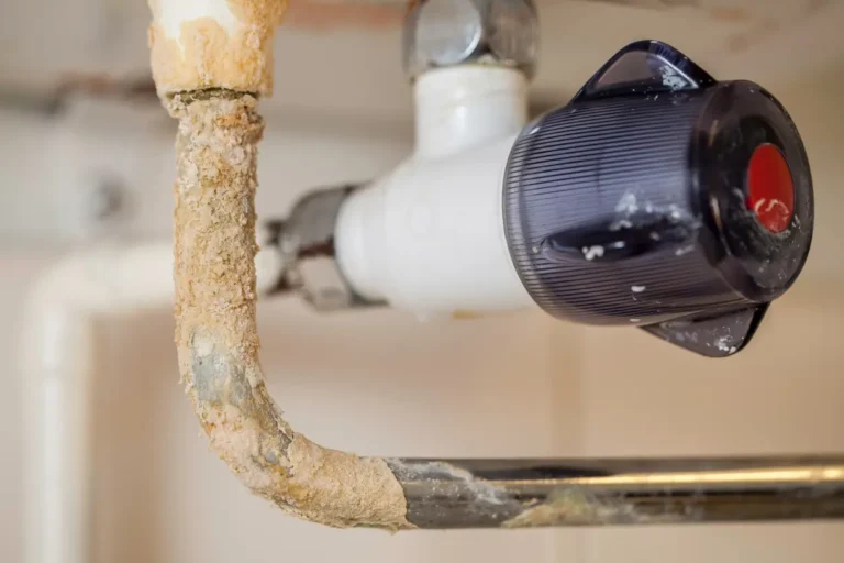 Hard water plumbing damage showing mineral buildup and corrosion on metal pipe under sink from hard water exposure.